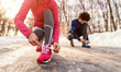 Close up of woman tying shoelace while kneeling and preparing for running. In background her friend tying shoe.Wintertime.