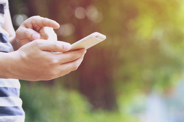 Close up of a man hand holding using mobile smart phone outdoor cellphone in public park. with filter Tones vintage effect ,Warm tones.