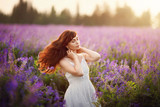 Fototapeta Tulipany - Outdoor portrait of a beautiful middle aged woman in a flowered field. The blossoming a galega a medicinal Galega officinalis. Purple flower. Happy young lady and spring summer nature, harmony concept