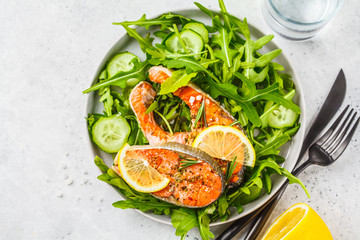 Canvas Print - Fried red fish with arugula and cucumber salad in white plate, copy space.