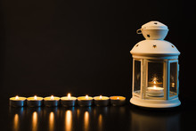 Several Small Burning Candles And A White Lantern With A Candle On A Black Background
