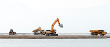 Bulldozers, Trucks Do Construction Work On The Background Of The Sea