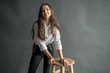 © Jurii - young pretty cute charming seductive girl standing next to a wooden chair on a gray background in a white shirt with loose hair