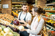© rh2010 - Shop worker helping young woman client to chooose vegetables in the supermarket