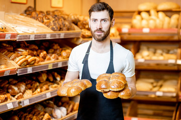 Wall Mural - Portrait of a handsome baker in uniform standing with fresh pastries in the bakery deparment of the supermarket