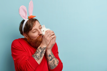 Wall Mural - My lovely pet, I love you! Affectionate ginger man lover of animals kisses and keeps to face small white rabbit, wears ears as if bunny, has tattoo, dressed casually, feels joy to play with hare.