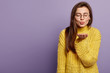 © wayhome.studio  - Portrait of lovely young woman keeps lips folded, stretches hands, makes air kiss, sends love on distance, wears spectacles and yellow knitted sweater, stands over purple wall, blank space on left