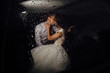 The bride and groom kissing in the car late at night, and it's raining outside. Bride and groom photographed behind the wet glass