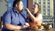 © motortion - Smiling woman treating boyfriend french fries, fat couple date, unhealthy food