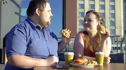 Obese man and woman sharing burgers during romantic date outdoors, calories