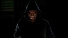 Hacker In Hoodie Using Laptop And Looking Into Camera With Evil Eyes, Malware