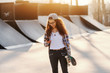 © dusanpetkovic1 - Skinny mixed race teenage urban girl using smart phone and holding skateboard while standing at skate park.