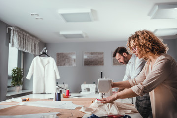 Professional tailors during work on project in fashion design studio, using sewing equipment