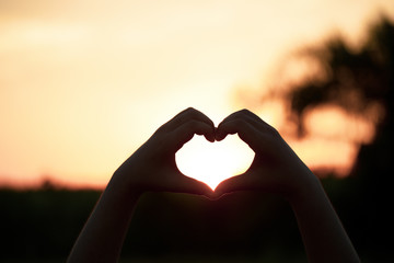 Beautiful Silhouette hand made heart shape on the sunset background.