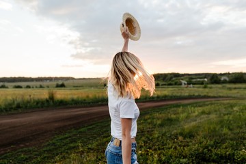 Wall Mural - Young girl raised up hat standing on the lawn watching the sunset holiday Season in warm places