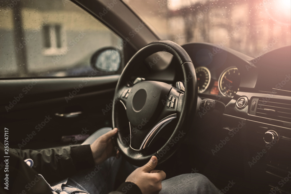 driver’s hands hold the steering wheel of a modern car while waiting for a passenger.