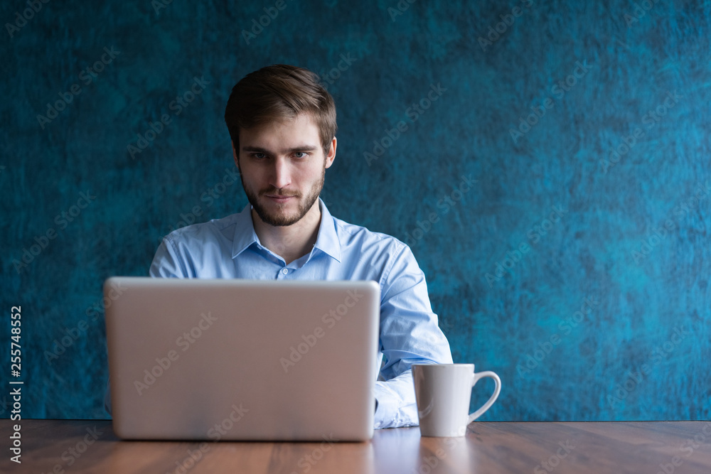 Happy young businessman using laptop at his office desk. - obrazy, fototapety, plakaty 