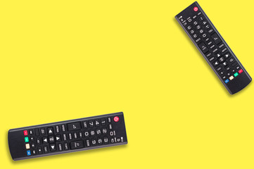 Pair of black plastic remote controls for different multimedia devices on yellow background with copy space for your text. Top view