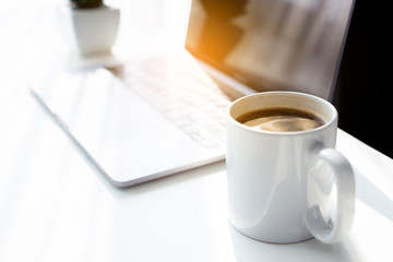 Business workspace with laptop on white table in the morning sun light, Coffee cup in the working time