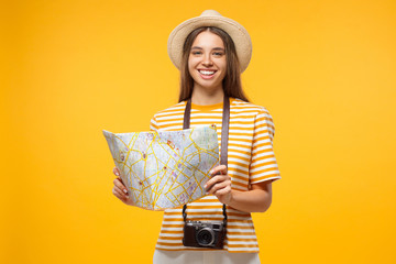 Young cheerful female tourist holding oldschool paper map, isolated on yellow background