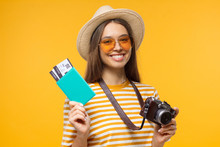 Excited Cheerful Young Tourist Girl Holding Passport With Tickets And Camera, Isolated On Yellow Background