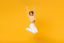 Successful Young Female Acts Like Winner, Jumping High In The Air With Hands Up, Isolated On Yellow Background