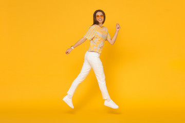 Wall Mural - Happy young woman jumping like she walking in the air, isolated on yellow background