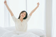 © whyframeshot - white dress asian beautiful woman stretching morning wake up bedroom with white curtain background lifestyle home concept