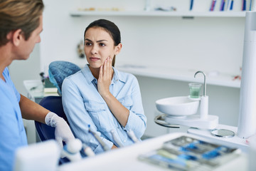 Wall Mural - Young lady having toothache and looking at dentist