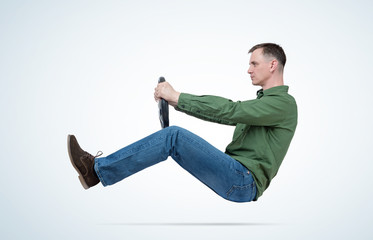 Man in green shirt and jeans drives a car with a steering wheel. Auto driver concept