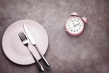 Alarm clock and plate with cutlery. Concept of intermittent fasting, lunchtime, diet and weight loss