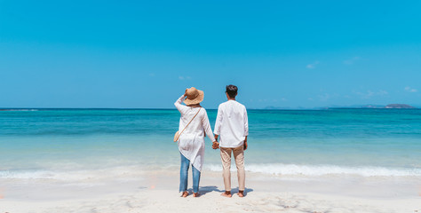 Wall Mural - Young happy couple white dress on seashore. Travel Vacation Retirement Lifestyle Concept. young couple hugging and turn back on the beach in vacation day. summer time.