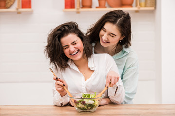 Two young women cooking and hugging at kitchen.