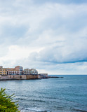 Fototapeta Na drzwi - Wonderful view of the seafront of Ortigia in Syracuse on a summer day, with blue sea and cloudy sky as a backdrop.