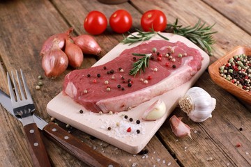 Meat - raw rumpsteak - rumpsteak  with rosemary, pepper, tomatos and spices on a rustic wooden table