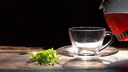 Wall Mural - Slow motion pouring tea in glass teapot and cup with steam on wood background