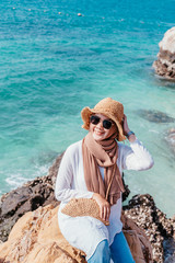 Wall Mural - Young confident muslim woman white dress catching a hat on seashore. Travel Vacation Retirement Lifestyle Concept. asian woman wear sun glass looking on the beach in vacation day. summer time.