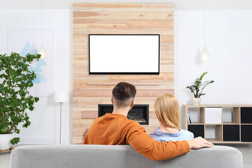 Wall Mural - Couple watching TV on sofa in living room with decorative fireplace