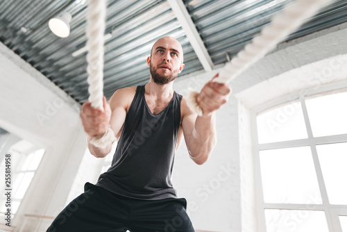 Fit Man Athlete Using Battle Ropes For Exercising At Light