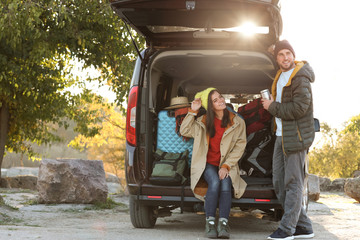 Poster - Young couple packing camping equipment into car trunk outdoors