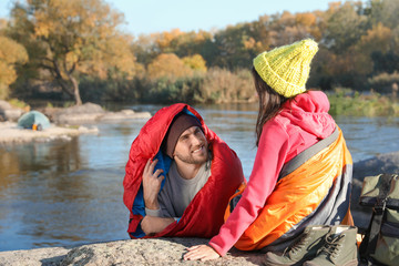 Wall Mural - Couple of campers in sleeping bags sitting on rock near pond. Space for text