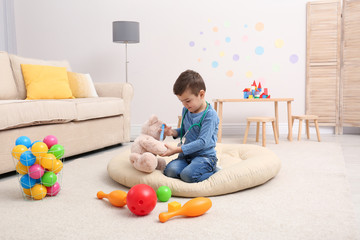 Wall Mural - Cute child playing doctor with stuffed toy on floor in hospital