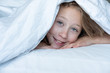 female child under duvet on bed looking out from underneath