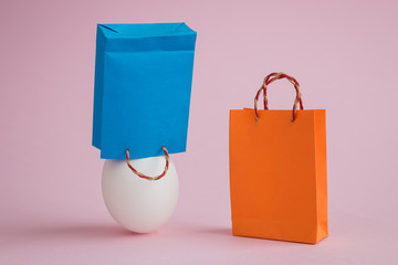 White egg with two shopping bags abstract on pastel pink background.