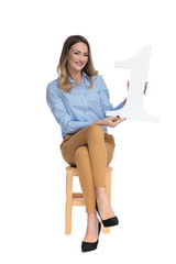 Sticker - young blonde businesswoman holds number one sign while sitting