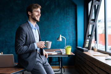 Happy attracive young businessman drinking coffee in office.