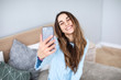 © BestForYou - Pretty smiling woman taking selfie using smartphone at home.