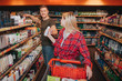 © estradaanton - Young couple in grocery store. Woman get deodorant from man. He stant at hygiene shelfs. People look at each pther and smile. Cheerful buyers.