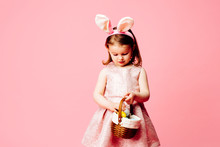 Portrait Of A Little Toddler Girl With Easter Bunny Ears And Basket Of Easter Eggs, Isolated On Pink
