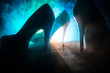 Artwork decoration. Silhouette of a man standing in the middle of the road on a misty night with giant high heel women shoes. Women power or women domination concept.